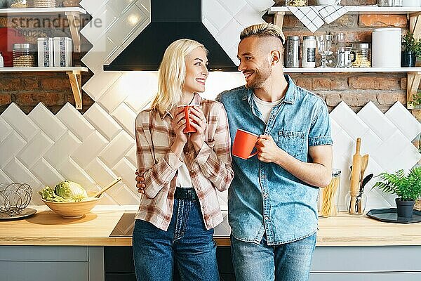 Junge glückliches Paar trinken Kaffee am Morgen und genießen die Gesellschaft von einander in der Küche zu Hause. Beziehung  Familie Konzept