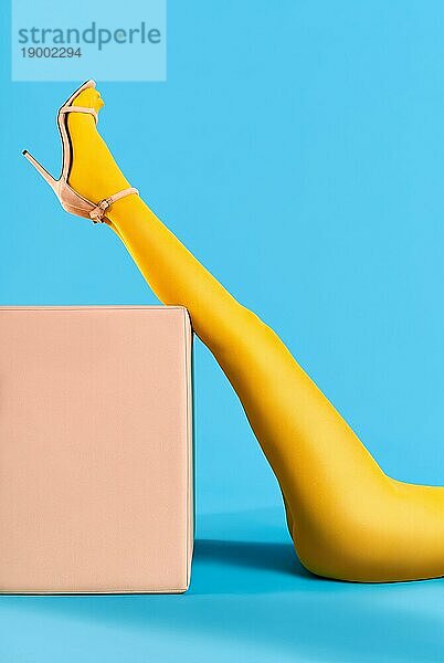 Schöne Frau mit perfekten Beinen in leuchtend gelben Strumpfhosen angehoben Beine auf blauem Hintergrund entspannen