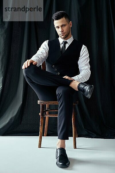Selbstbewusster gutaussehender Mann in elegantem Anzug posiert auf einem Stuhl sitzend. Retrostil