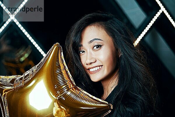 Porträt einer hübschen lächelnden asiatischen Frau  die Spaß hat und einen goldenen Luftballon hält. Party Zeit  Feier Konzept