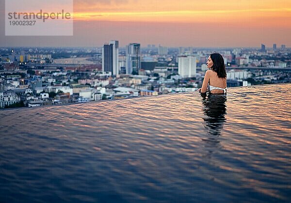 Junge Frau entspannen im Schwimmbad auf dem Dach während erstaunlichen Sonnenuntergang und genießen Sie den Blick auf die Stadt. Sommerurlaub und Ferien Konzept