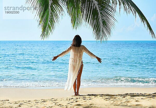 Rückenansicht der freien jungen Frau entspannen und genießen Meer stehen unter Palme am tropischen Strand. Sommerurlaub Konzept