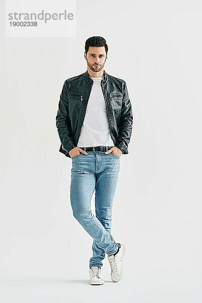 Handsome stilvollen Männchen Porträt auf weißem Hintergrund Studio. Men's Schönheit Konzept. Junger Männchen trägt Jeans  weißes TShirt und schwarze Lederjacke posiert in voller Länge