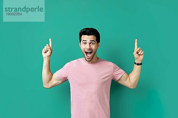 Gutaussehender  glücklicher Mann zeigt mit dem Finger auf leeren Kopierraum  vorblauem Hintergrund. Präsentiert Produkt und Werbekonzept
