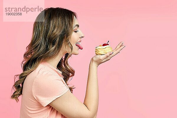 Profil Porträt der jungen Frau lecken köstliche Gebäck Kuchen auf rosa Hintergrund mit Kopie Raum