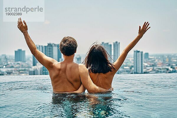 Junges  glückliches  verliebtes Paar mit erhobenen Armen  das Spaß im Schwimmbad hat. Sommerurlaub  Flitterwochen  Reisekonzept. Rückansicht