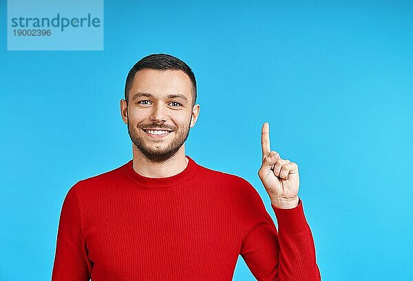 Gutaussehender  glücklicher Mann zeigt mit dem Finger auf leeren Kopierraum  vorblauem Hintergrund. Präsentiert Produkt und Werbekonzept