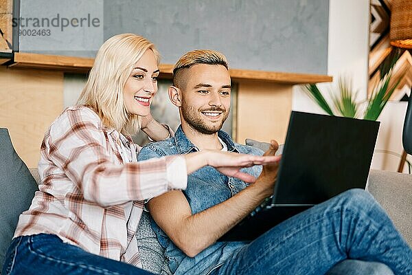 Fröhliches junges Paar mit Laptop  das im Internet surft und zu Hause auf dem Sofa sitzt