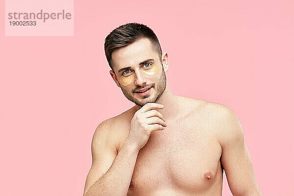 Porträt eines lächelnden gut aussehenden Mannes mit goldenen Augenklappen auf rosa Hintergrund. Männer Schönheit  Hautpflege Konzept