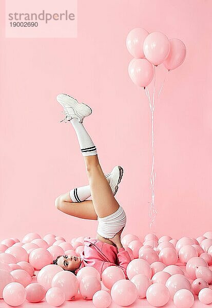 Junge hübsche Frau haben Spaß mit den Beinen nach oben in rosa Ballons über rosa Pastell Hintergrund liegen. lustige kreative Konzept