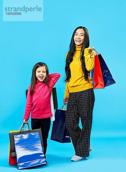 Glückliche Mutter mit entzückenden kleinen Tochter hält Einkaufstaschen genießen ihren Kauf auf blauem Hintergrund. Spaß  Verkauf  Familie Konzept