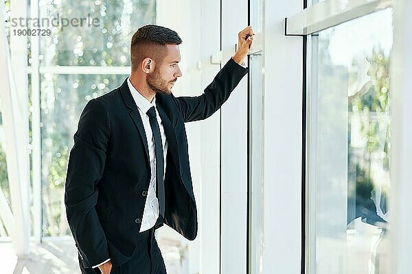 Profilansicht eines selbstbewussten Geschäftsmannes in einer eleganten Suite in einem modernen  kreativen Büro mit Blick durch die Panoramafenster