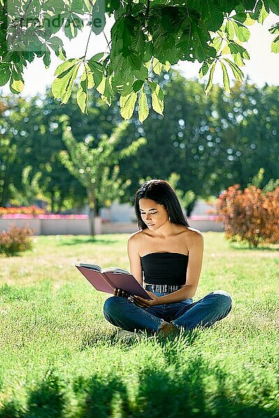 Hübsche afroamerikanische Frau liest Buch auf Gras im Park. Entspannen und Hobby Konzept