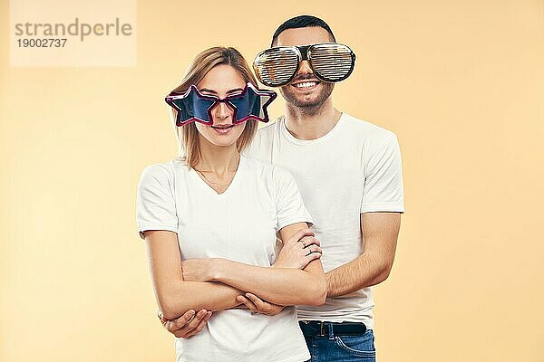 Junges glückliches Paar in lustiger Partybrille auf beigem Hintergrund. Spaß Konzept