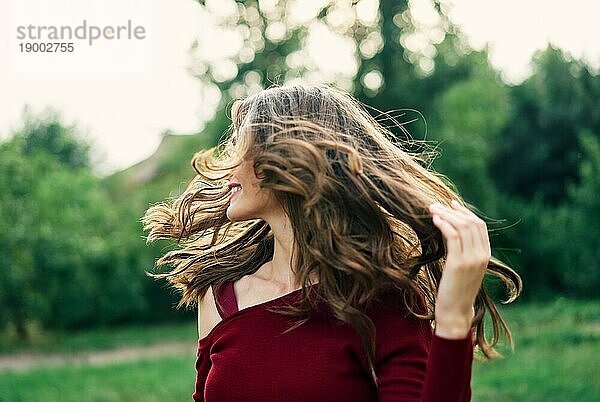 Junge glückliche Frau mit flatternden Haaren haben Spaß im Freien auf grünen Sommer Natur Hintergrund. Weibliche Schönheit Konzept