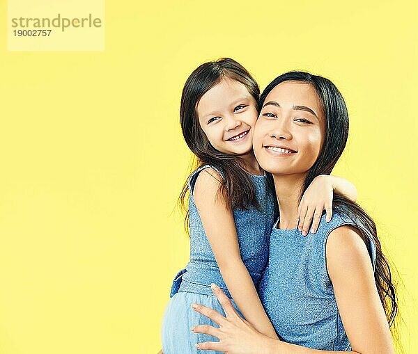 Glückliche Mutter und ihr Kind Tochter umarmen auf gelbem Hintergrund. Familie  umarmen Konzept