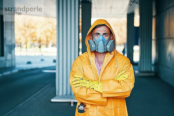 Nahaufnahme eines jungen Mannes mit Atemschutzmaske und gelbem Regenmantel  der auf der Straße posiert und in die Kamera schaut