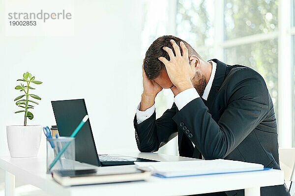 Gestresste müde Geschäftsmann sitzt am Schreibtisch in kreativen Büro. Mann leiden unter Kopfschmerzen  Probleme Konzept