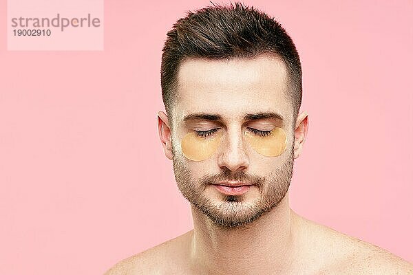 Junger hübscher Mann mit geschlossenen Augen und goldenen Augenklappen auf rosa Hintergrund. Männer Schönheit  Hautpflege Konzept