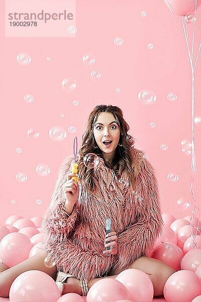 Junge hübsche Frau  die Spaß mit Seifenblasen auf rosa Hintergrund mit Luftballons. Party  Feier  Spaß Konzept
