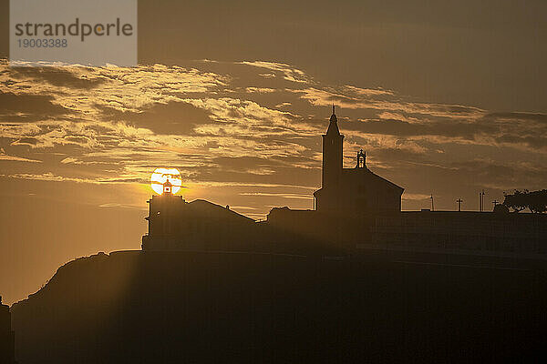 Sonne im Einklang mit der Silhouette des Leuchtturms und der Kirche von Luarca  Asturien  Spanien  Europa