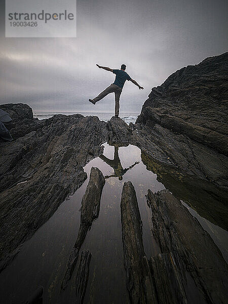 Ein Mann balanciert auf einem Bein auf den Felsen und sein Spiegelbild in einem Wasserteich  Spanien  Europa