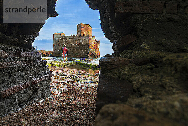 Blick von unten auf einen Mann  der vor der Burg von Torre Astura steht und durch ein Loch in der Mauer gesehen wird  Provinz Rom  Tyrrhenisches Meer  Latium (Latium)  Italien  Europa