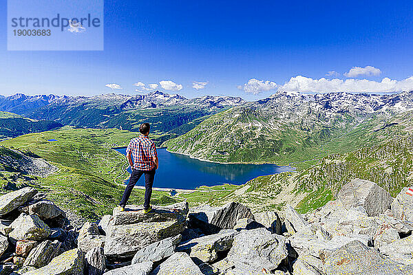 Ein Mann blickt auf den auf Felsen stehenden Alpensee Montespluga  Madesimo  Valle Spluga  Veltlin  Lombardei  Italien  Europa
