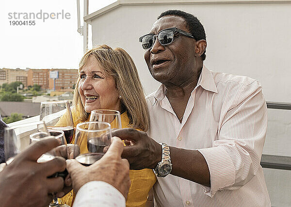 Ältere Männer und Frauen stoßen mit Freunden auf dem Balkon auf Wein an
