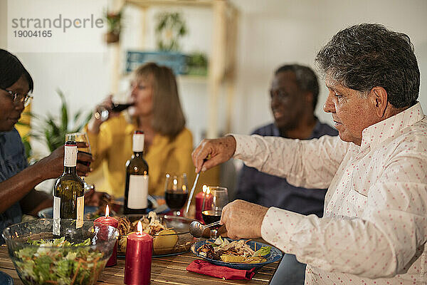 Senior man eating food with friends at dinner party