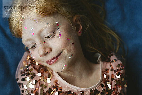Blond girl with crystals on face lying on blue fabric