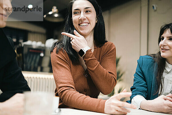 Glückliche Geschäftsfrau gestikuliert und redet mit Freunden im Café