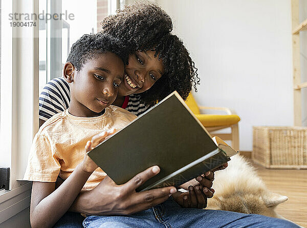 Smiling mother and son reading book together at home