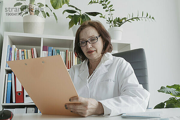 Senior doctor analyzing medical record at table in office