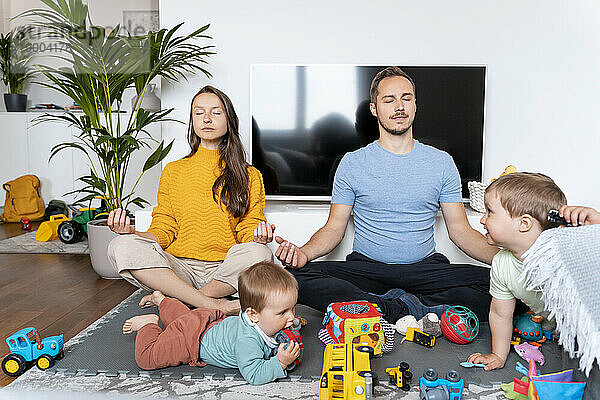 Eltern meditieren mit Kindern  die zu Hause im Wohnzimmer spielen