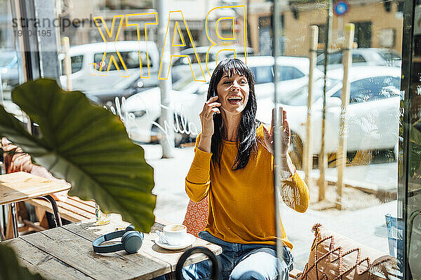 Glückliche reife Frau winkt und spricht im Café mit dem Smartphone