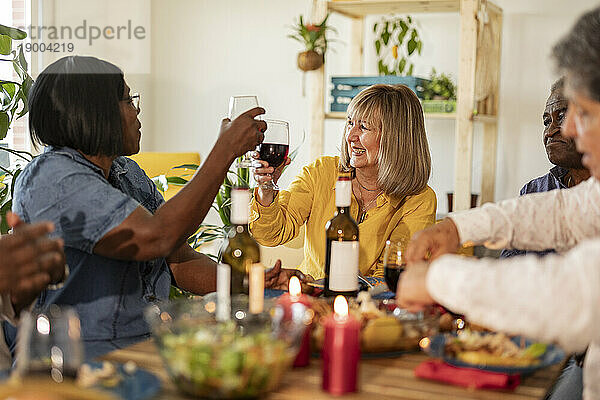 Glückliche ältere Frauen  die zu Hause mit Freunden Wein anstoßen