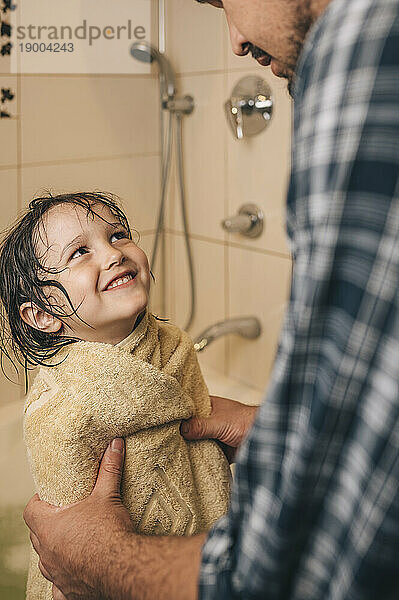 Happy boy wearing towel with father in bathroom