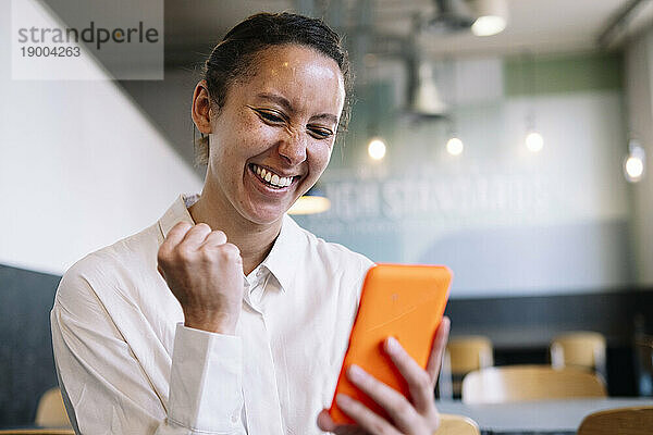 Fröhliche Geschäftsfrau benutzt Smartphone im Café