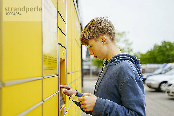 Blonder Junge mit Ticket gibt Daten in Paketschließfachautomat ein