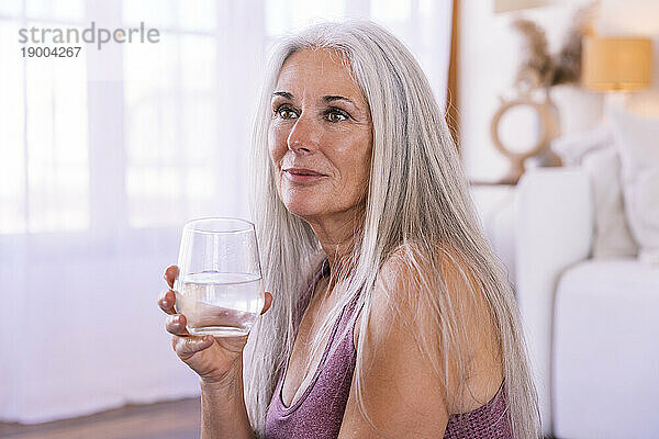 Reife Frau mit einem Glas Wasser zu Hause