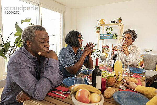 Multikulturelle ältere Freunde reden zu Hause am Esstisch miteinander