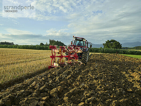 Landwirt pflügt Feld mit Traktor bei Sonnenaufgang