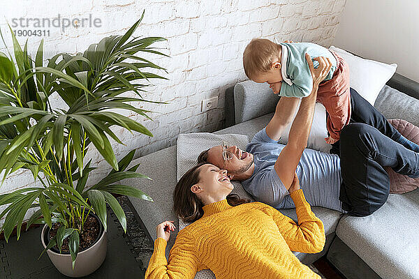 Happy parents spending leisure time with baby boy on couch at home