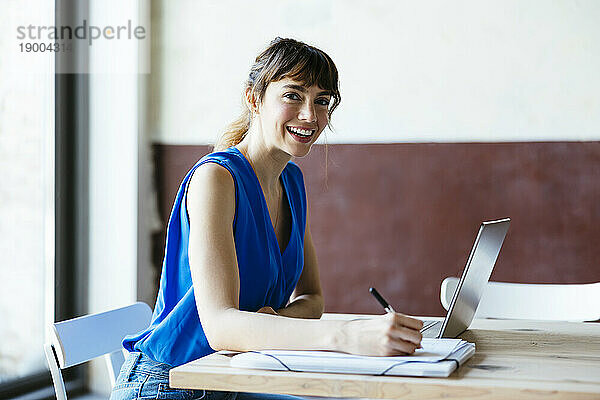 Glückliche Geschäftsfrau sitzt mit Laptop am Schreibtisch