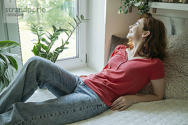 Glückliche junge Frau entspannt sich zu Hause auf dem Fensterplatz in der Nische