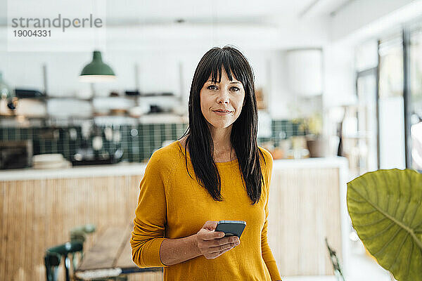 Reife Frau steht mit Mobiltelefon im Café