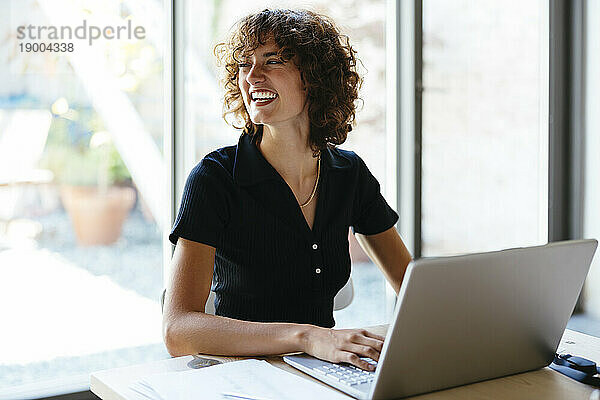 Glückliche junge Geschäftsfrau sitzt mit Laptop am Schreibtisch