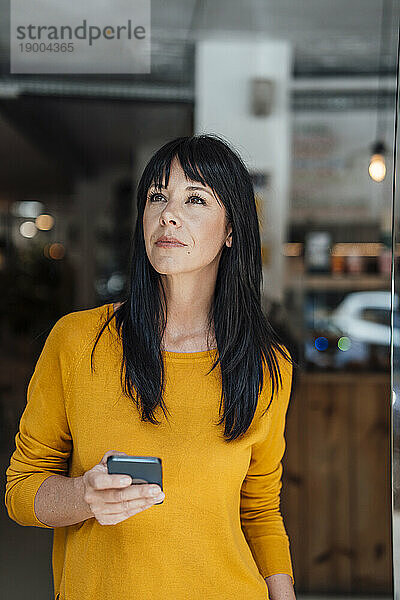 Nachdenkliche Frau steht mit Mobiltelefon