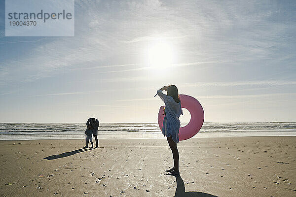 Frau hält an einem sonnigen Tag einen aufblasbaren Schwimmring am Strand